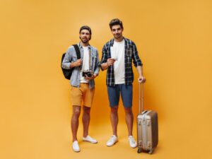 Fulllength Portrait Brunet Handsome Men Colorful Shorts Checkered Shirts White Tshirts Hold Suitcase Tickets Retro Camera Travelers Pose Orange Background 300x225