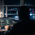 A person is coding on a laptop at night.